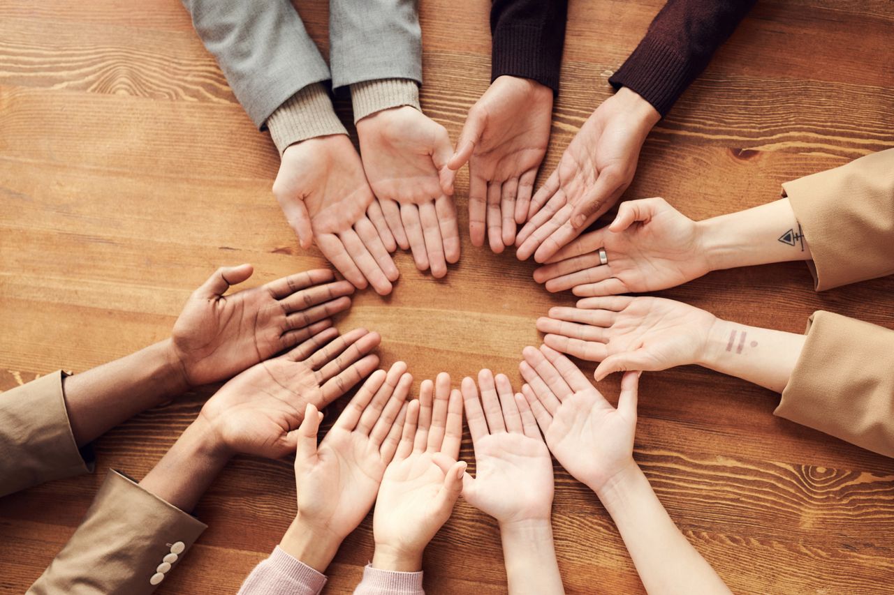 about-us Top view of diverse hands forming a circle on a wooden table, symbolizing unity and diversity.