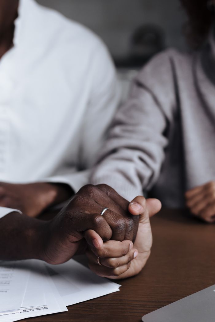 our-story A diverse couple holding hands over documents on a table indoors.